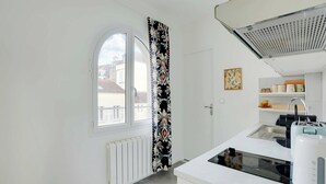 Una cucina moderna con mobili bianchi, forno integrato e una finestra con tenda a motivi bianchi e neri.
