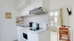 Una cucina compatta con piano cottura integrato, macchina da caffè e un piccolo angolo ristoro con una sedia e un tavolo.
