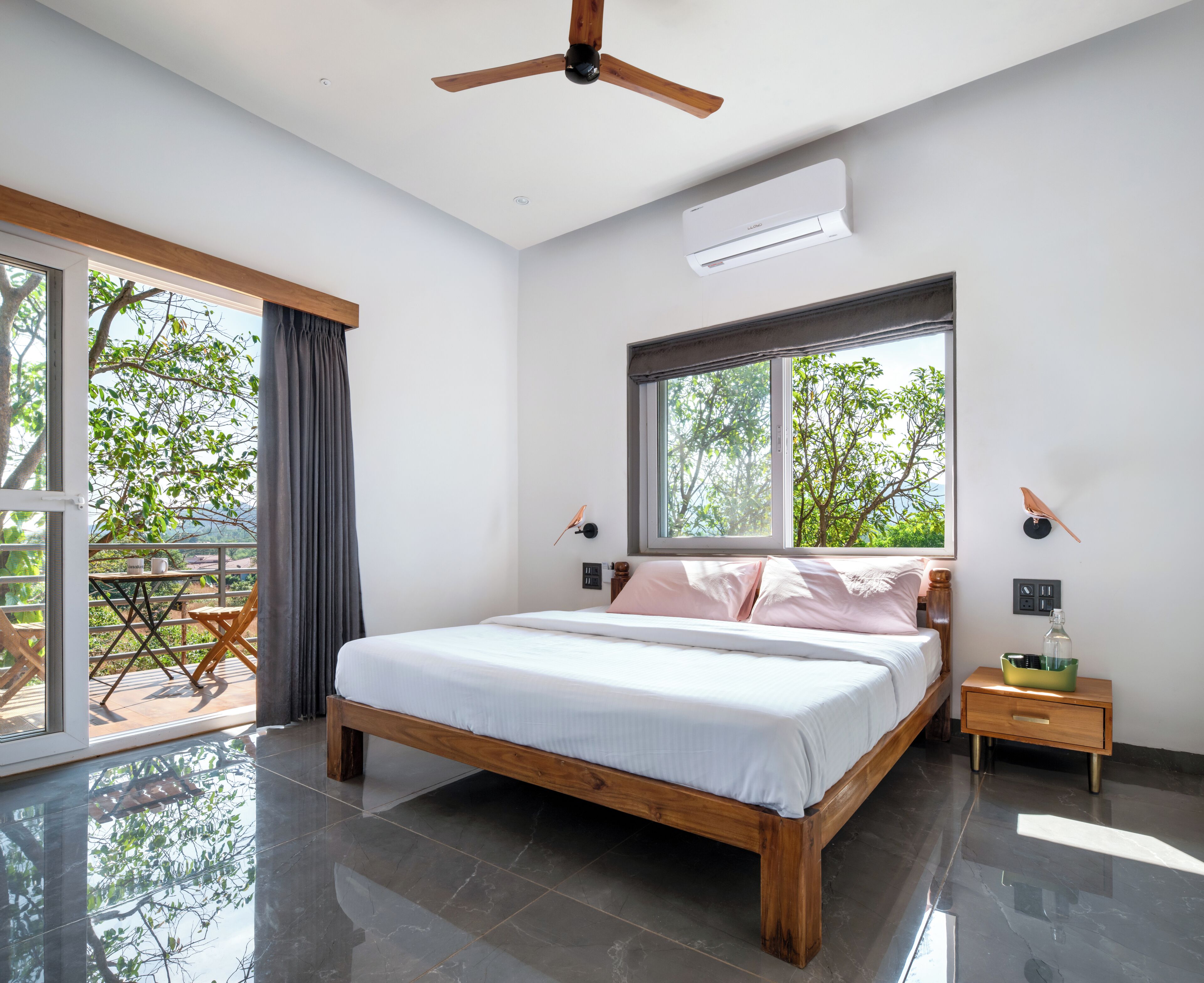 Un dormitorio moderno con una cama grande, ventilador de techo, unidad de aire acondicionado y vistas a árboles a través de una ventana.