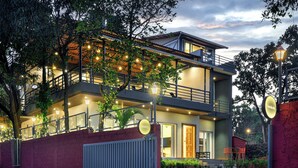 A two-story building with a balcony, a gated entrance, and string lights. - Villa Vanakothi by Westbay (Shahuwadi)
