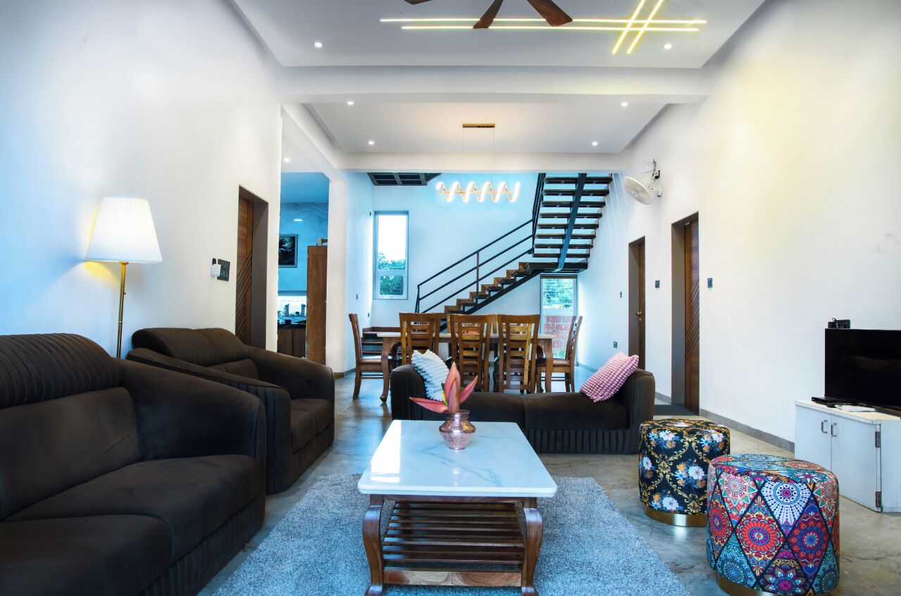 A modern living room with dark sofas, a coffee table, and a TV. There is a staircase leading to an upper floor.