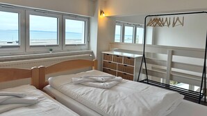 Et hotelværelse med en seng, et lille skrivebord, en stol, en radiator og et vindue med havudsigt.