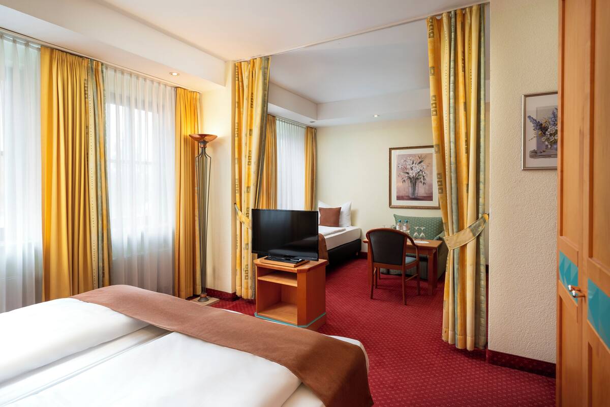 A hotel room with a bed, a desk with a computer, a chair, and a TV.