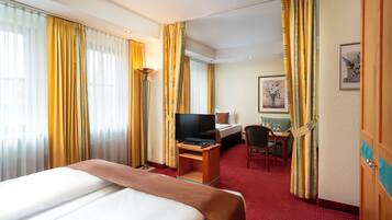 A hotel room with a bed, a desk with a computer, a chair, and a TV.