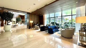 A spacious lobby with a polished floor, seating area with sofas, a large potted plant, and a view of the outside through large windows. - 3BHK Luxury Living at The Address Opera  (Dubai)