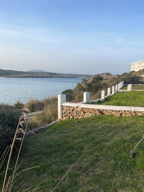 A coastal landscape with a stone wall and a grassy area leading to a body of water.