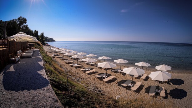 A beach with sun loungers and umbrellas, a wooden deck with chairs, and a view of the sea. - Crown Hotel  (Kassandra)