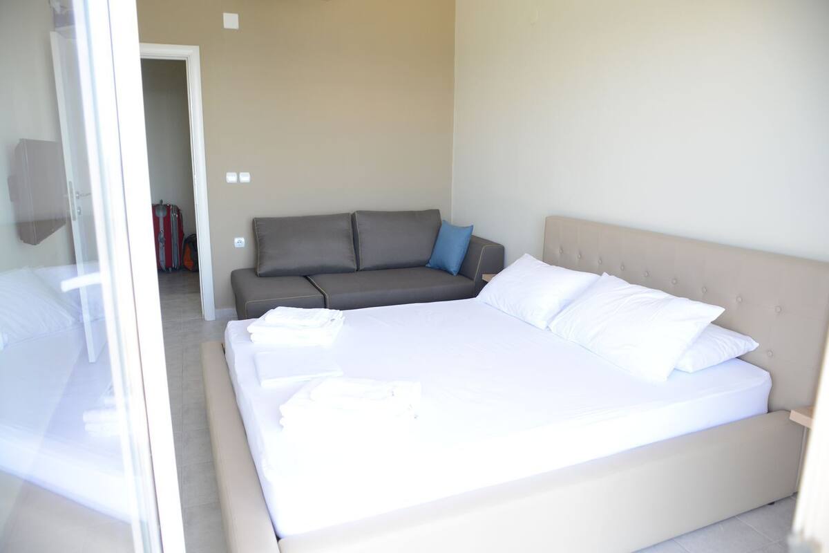 A bedroom with a large bed, a grey sofa, and a small table.