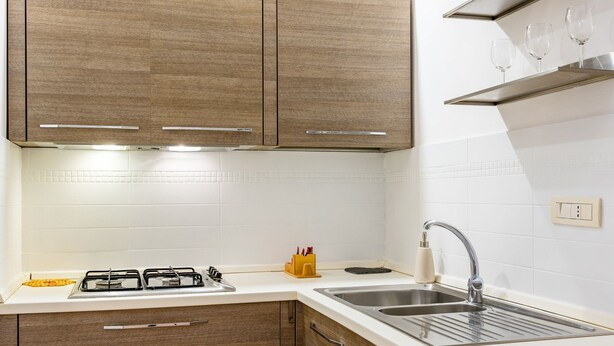 A modern kitchen with wooden cabinets, a white countertop, a gas stove, and a stainless steel sink. - Materdei Terrace by Napoliapartments (Naples)