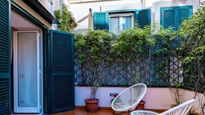 A courtyard with orange tiled flooring, white wicker chairs, and a lattice wall with greenery. - Materdei Terrace by Napoliapartments (Naples)