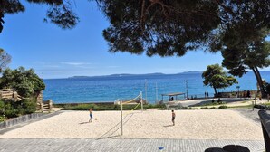 Una cancha de voleibol de playa con red, rodeada por una terraza de madera y un muro de piedra.