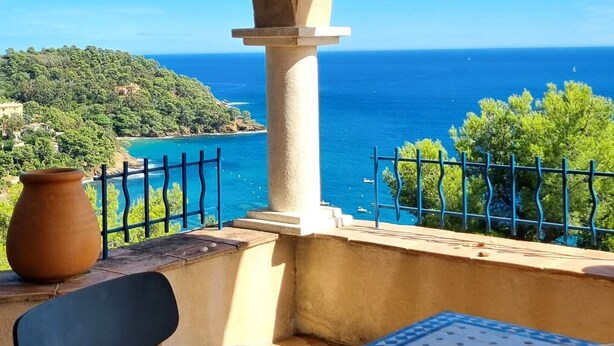 Una terraza con una mesa lista para dos personas, con vistas a un paisaje costero y cielos despejados.