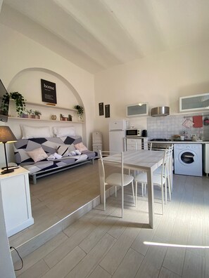 A modern kitchen with a dining area, a sofa, and a washing machine. - Accogliente bilocale - Volsci 153 (Rome)