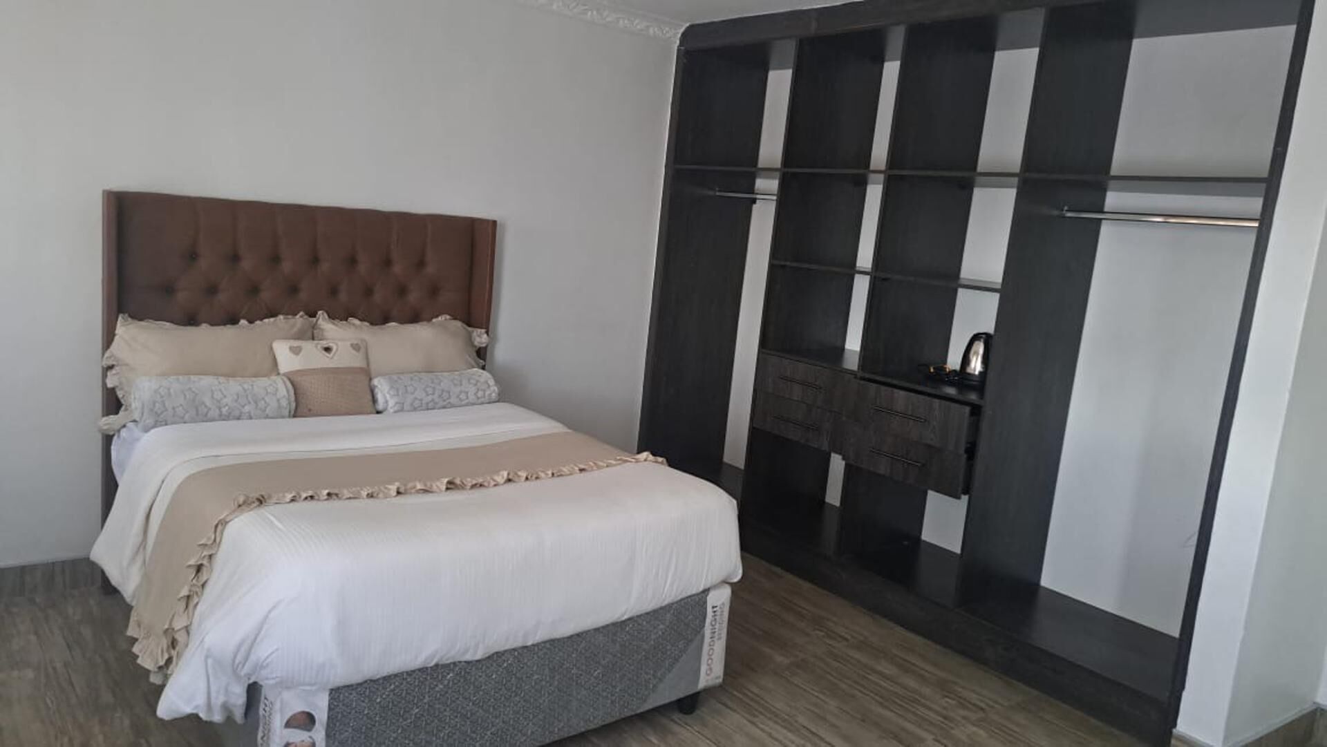A bedroom with a large bed, a wardrobe with multiple compartments, and a small shelf with a kettle.