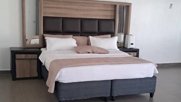A modern hotel room with a large bed, a nightstand, a bedside table, and a wall-mounted air conditioning unit. - Gletwyn House Retreat in Harare (Harare)