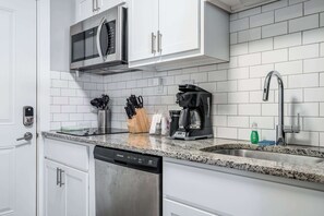 A modern kitchen with white cabinets, a stainless steel dishwasher, a microwave, a coffee maker, and a sink with a faucet. - 18BR 17BA Combined Apartments close to Lucas Oil Stadiom (Indianapolis)