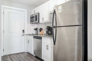 Una cocina moderna con armarios blancos, electrodomésticos de acero inoxidable y un refrigerador negro.