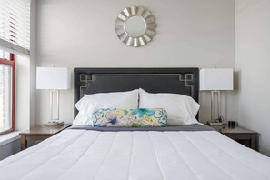 A neatly made bed with a floral pillow, two bedside lamps, and a round mirror on the wall.