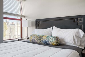 A neatly made bed with white linens, a decorative pillow, and a black headboard with a geometric design.
