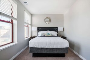 A bedroom with a bed, two bedside tables, a wall clock, and a window with blinds. - 18BR 17BA Combined Apartments close to Lucas Oil Stadiom (Indianapolis)