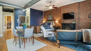 Una sala de estar moderna con pared de ladrillo, televisor de pantalla plana, chimenea y comedor con mesa y sillas.