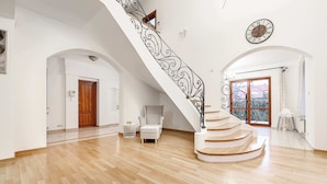 A spacious room with a wooden floor, a white staircase with a black railing, a wooden door, and a large window with a view. - Lumina amazing house in Warsaw (Warszawa BIG)