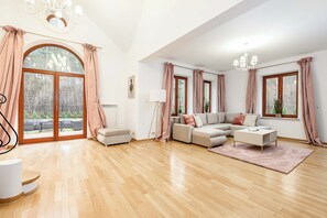 Un salón espacioso con suelo de madera, un conjunto de sofás, una mesa de centro y ventanas amplias con cortinas.