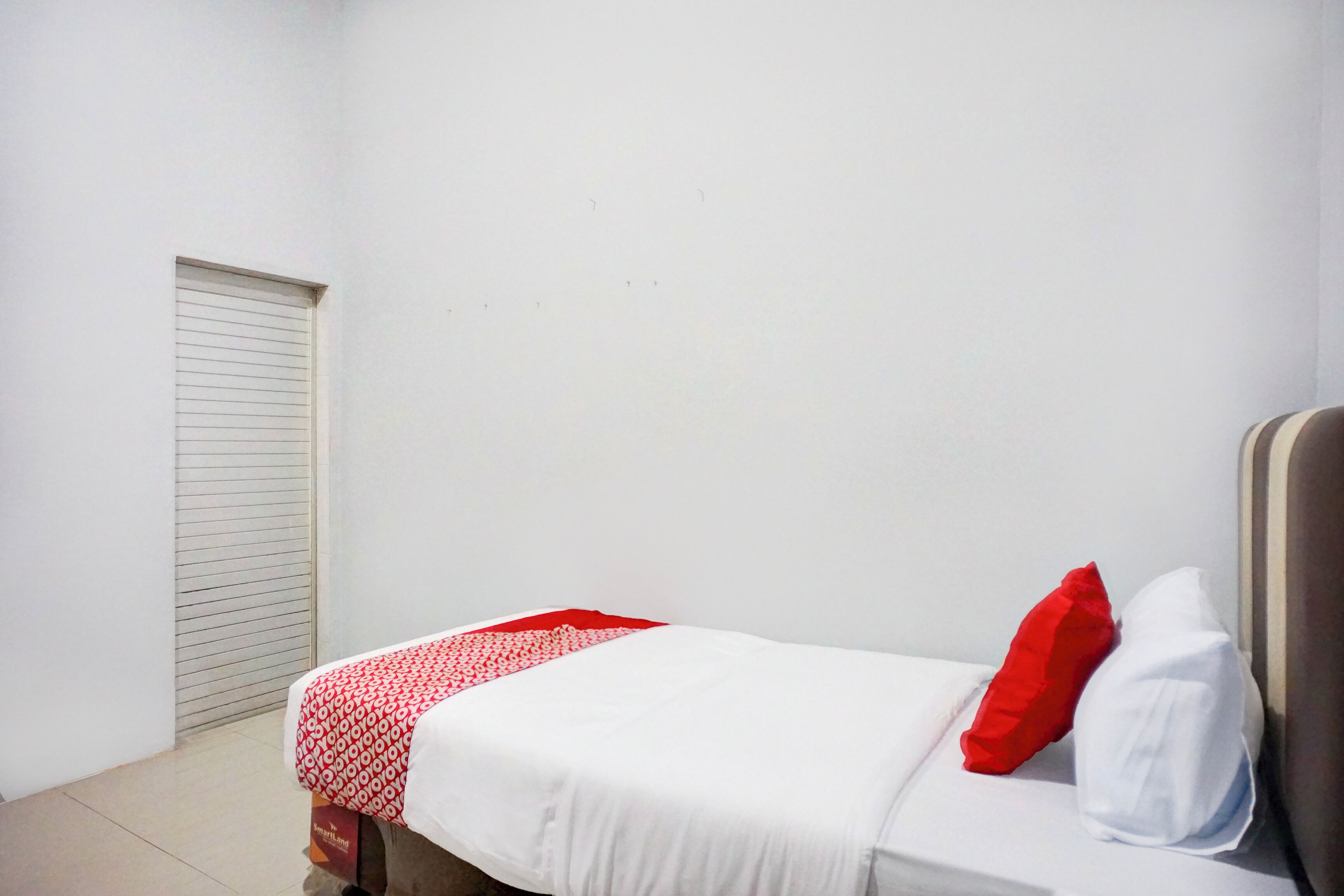 Une petite pièce propre, avec un lit simple, une porte fermée et un mur blanc.