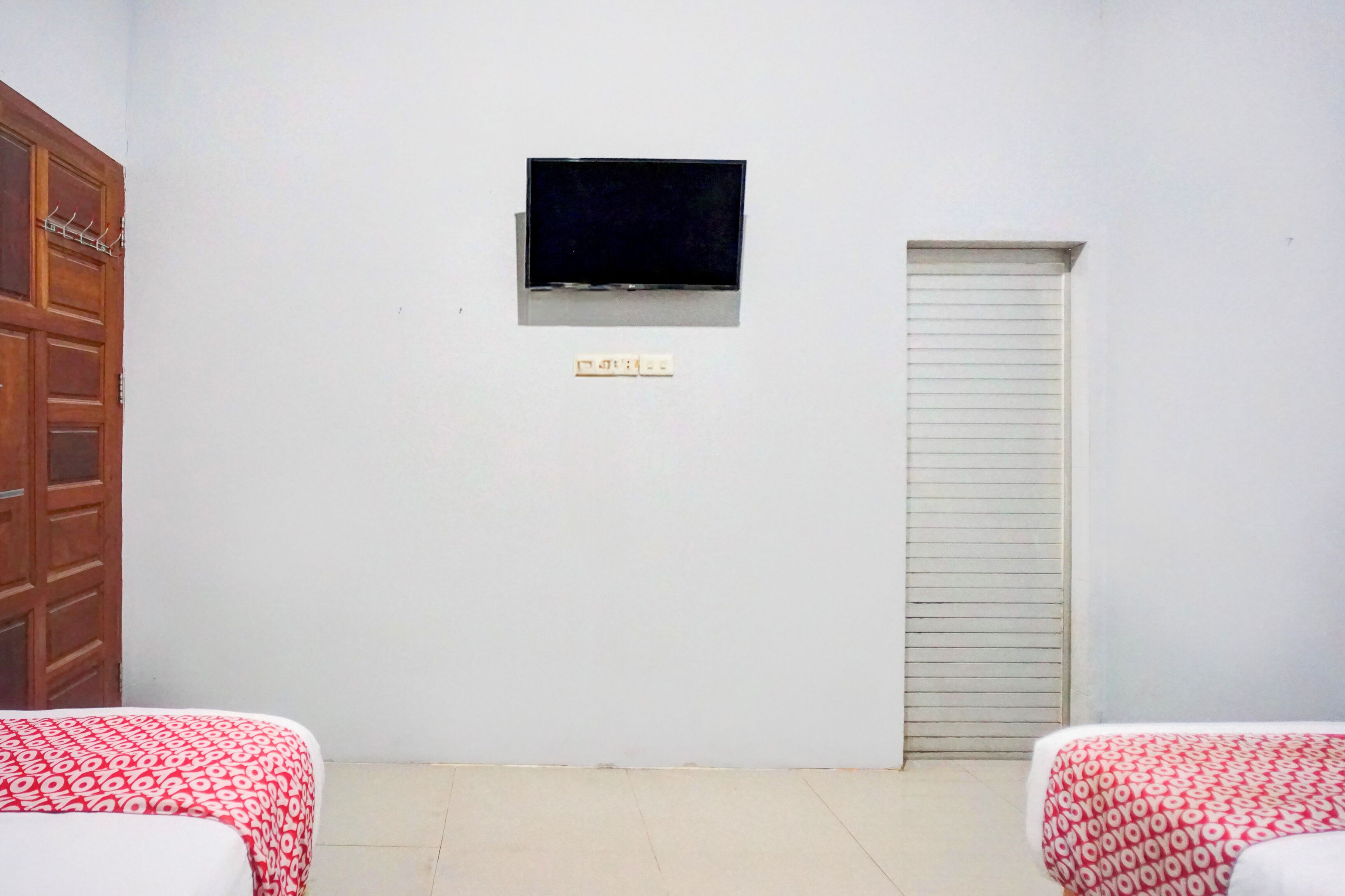 A room with two beds, a TV mounted on the wall, a door, and a small window.