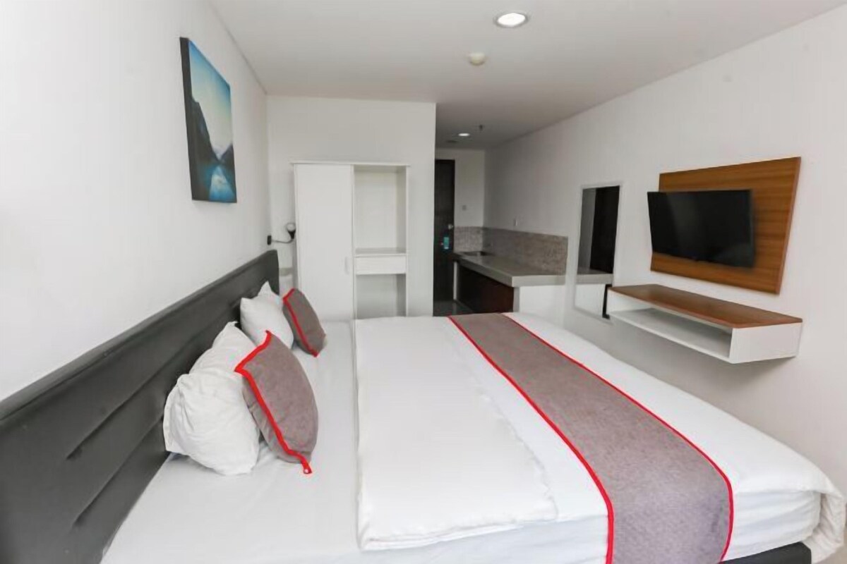 A modern hotel room with a large bed, a TV mounted on the wall, and a small desk area.