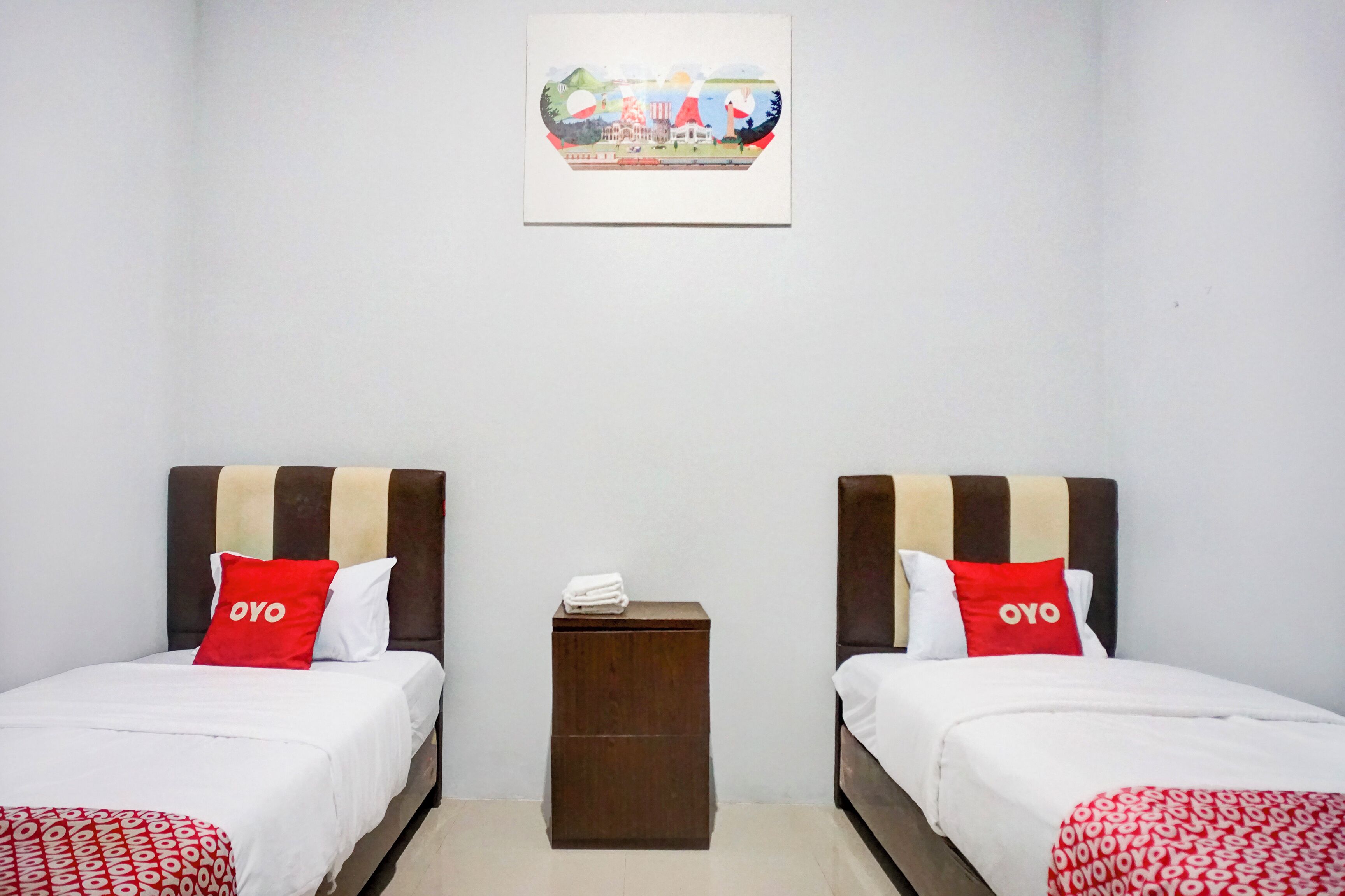 A hotel room with two beds, each with a headboard, a small bedside table, and a wall-mounted picture.