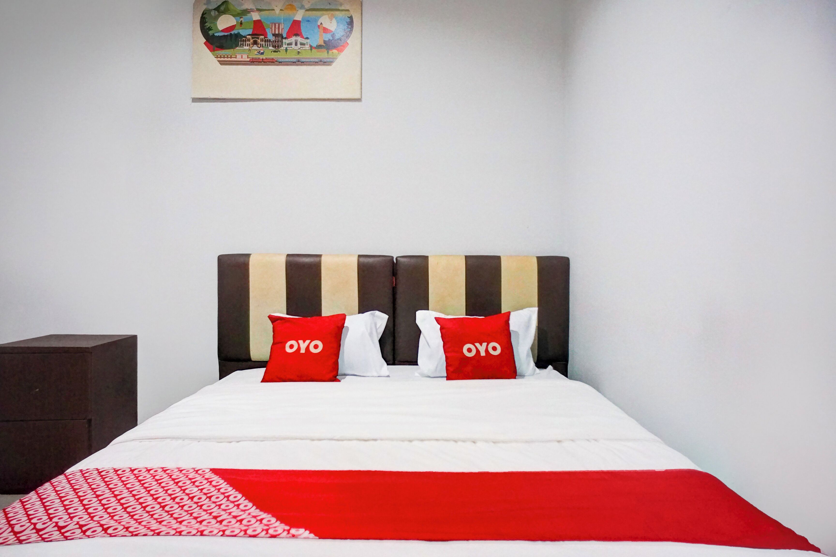 A neatly made bed with a striped headboard, two red pillows with the word "OYO" on them, and a red and white patterned throw blanket.