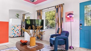 A modern living room with a TV, a blue chair, a table with a bowl of fruit, and a colorful rug. - Retro Rewind, Stylish, Near Design District Miami (Miami)