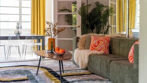 A living room with a sofa, a coffee table with a bowl of fruit, a dining area with chairs and a table, and a large plant. - Retro Rewind, Stylish, Near Design District Miami (Miami)