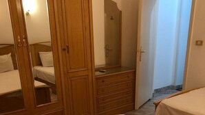 A bedroom with two beds, a wooden wardrobe, and a mirror.