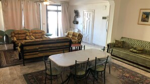 A living room with a striped sofa, a green sofa, a dining table with chairs, and a patterned rug.