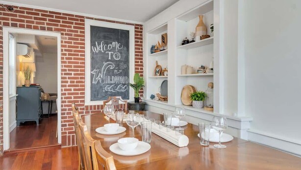 Un comedor con pared de ladrillo, un cartel de pizarra y un estante blanco con objetos decorativos.