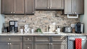 Una cocina con armarios oscuros, salpicadero de piedra y varios electrodomésticos, incluyendo una cafetera, un tostador y una tetera.