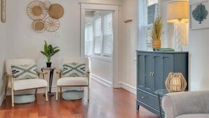 Una sala de estar con dos sillones, una mesita con una planta, un aparador y decoración en la pared.