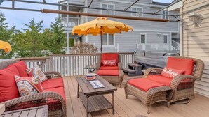 An outdoor patio with wicker furniture, red cushions, and a wooden table. - Beachy Keen Steps to Sand, Miles from Stress (Avalon)