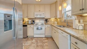 A modern kitchen with white cabinets, stainless steel appliances, granite countertops, and pendant lighting. - Beachy Keen Steps to Sand, Miles from Stress (Avalon)