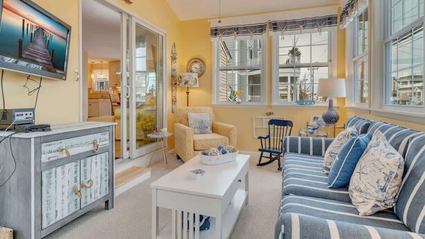 A cozy living room with a sofa, armchair, and a television on a cabinet. - Beachy Keen Steps to Sand, Miles from Stress (Avalon)