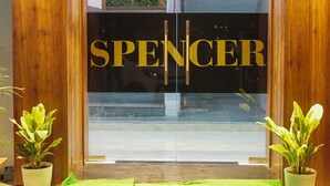 A hotel entrance with a green carpet, wooden walls, and the name 'SPENCER' on the glass doors. - Hotel Spencer- Kharghar Navi Mumbai (Panvel)