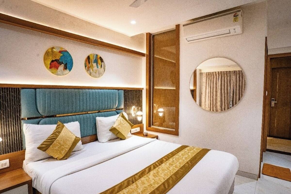 Hotellihuone, jossa on suuri sänky, pääty, yöpöydät, peili ja taideteos seinällä.