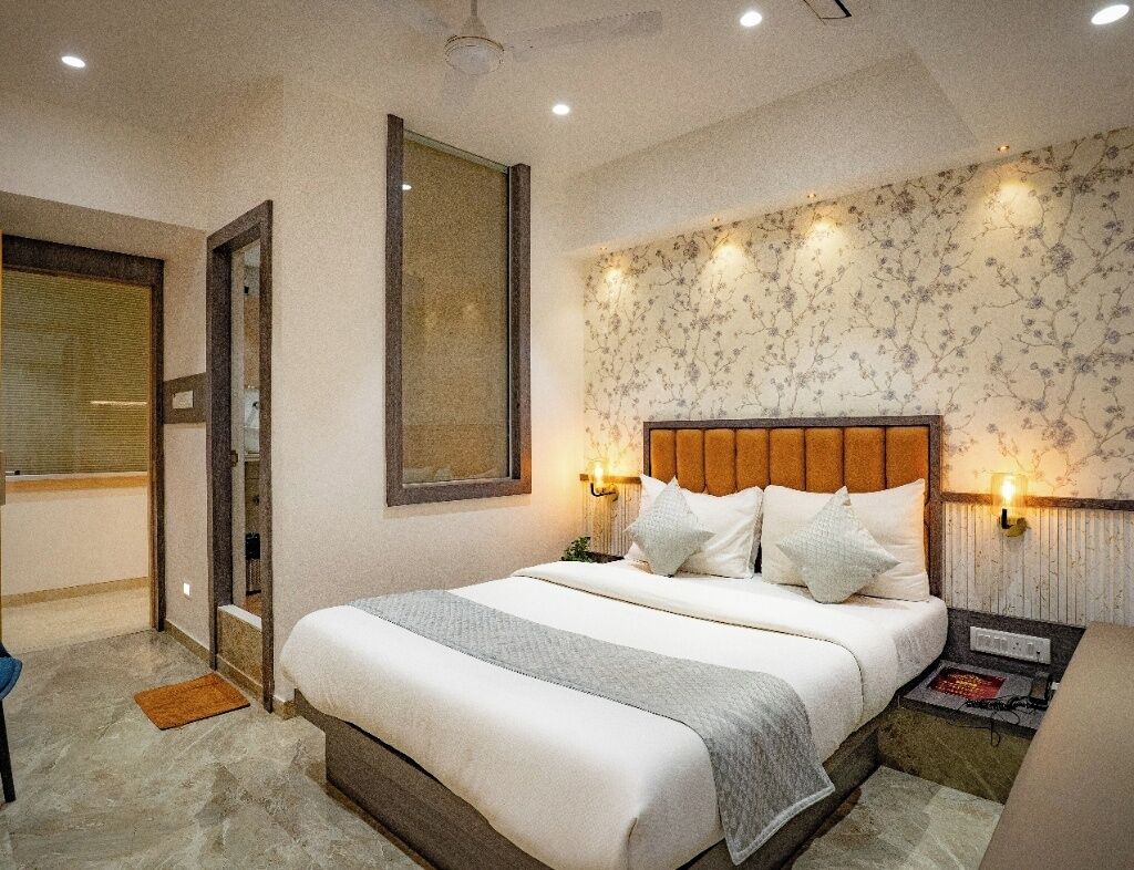 A hotel room with a large bed, a wooden headboard, two bedside lamps, a nightstand, and a window with blinds.
