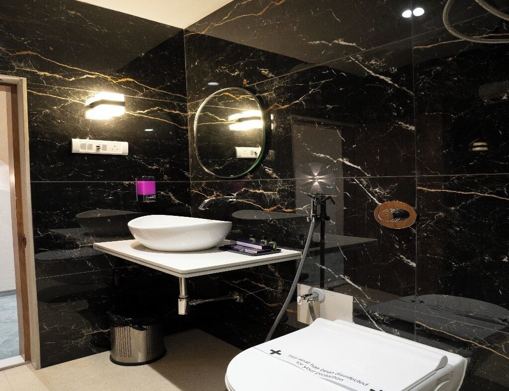 Ein modernes Badezimmer mit einem schwarzen Marmorwaschbecken, einem runden Spiegel und einer weißen Toilette.