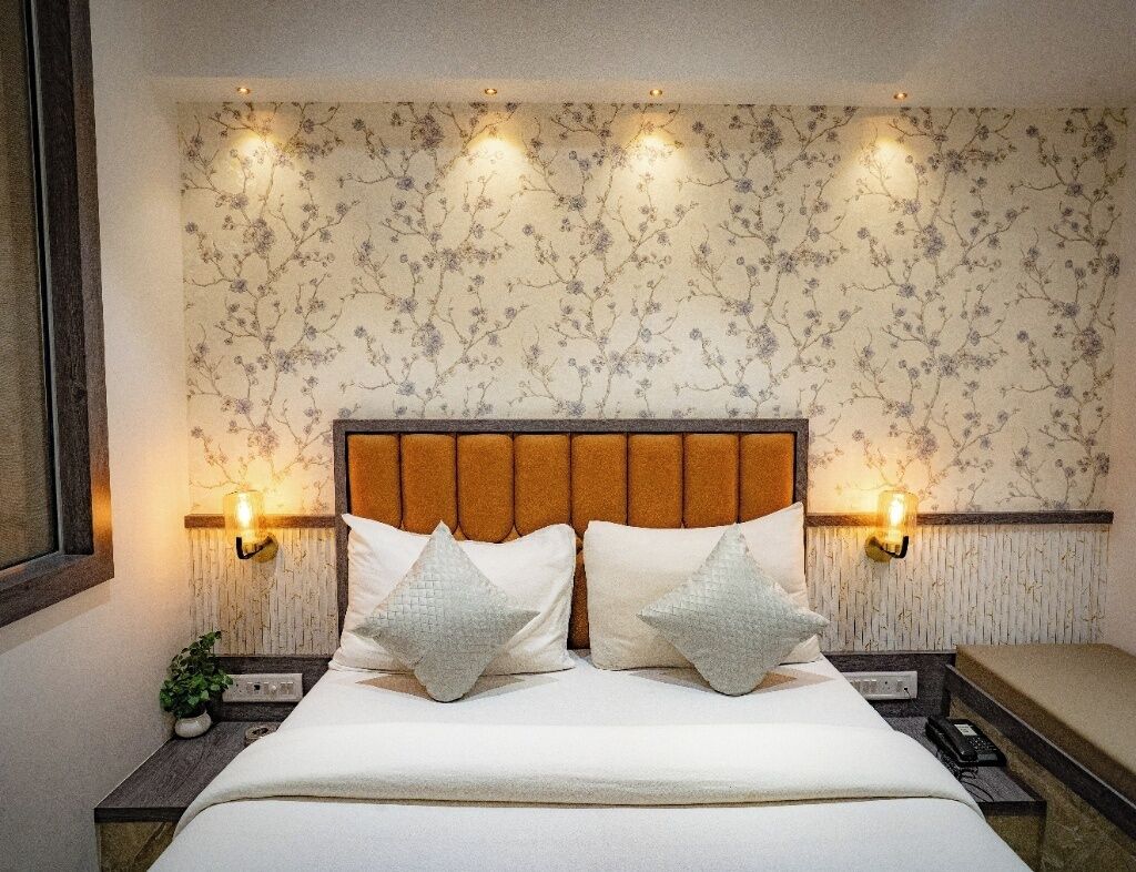 A neatly made bed with a wooden headboard, two bedside lamps, and a floral wallpaper pattern.