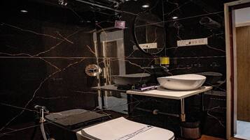Un baño moderno con pared de mármol negro, lavamanos blanco y un inodoro.