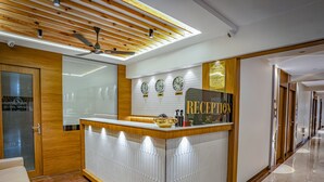 A hotel reception area with a wooden reception desk, a clock, and a sign that reads "RECEPTION". - Hotel Spencer- Kharghar Navi Mumbai (Panvel)