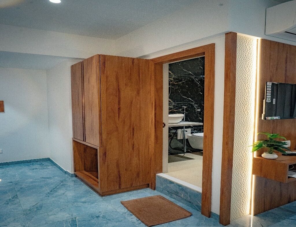 A modern bathroom with a wooden vanity, a marble sink, and a television mounted on the wall.